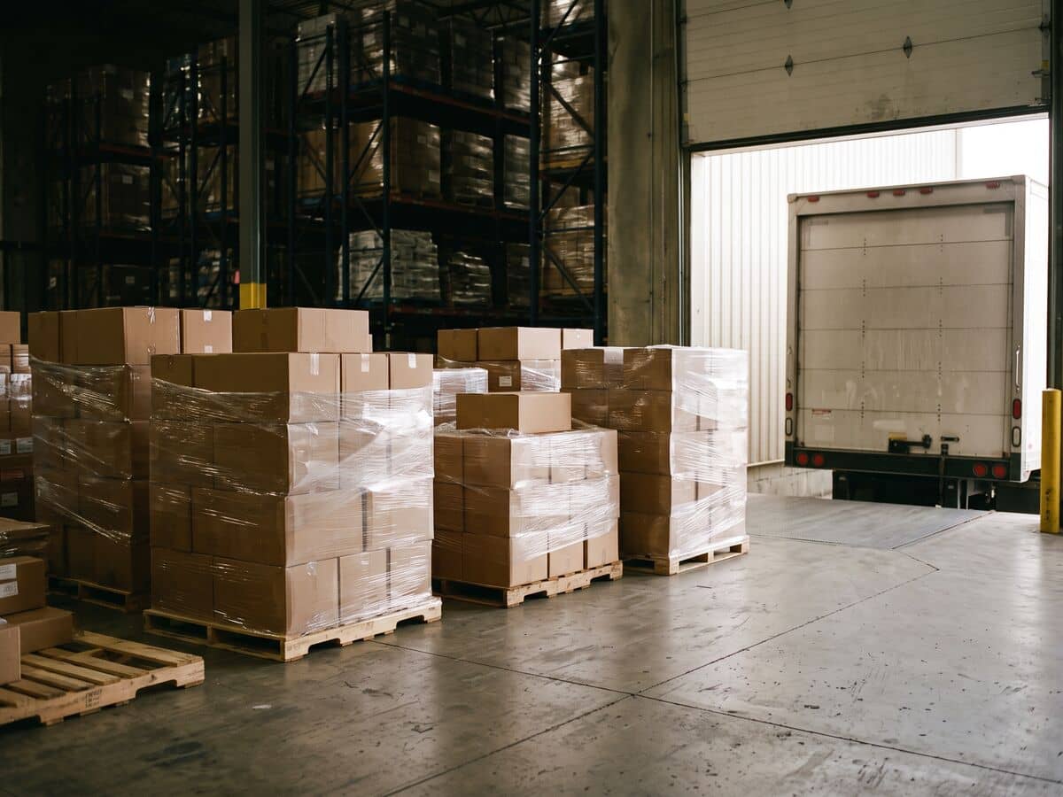 Shrink-wrapped pallets of apparel cartons on a warehouse loading dock beside a truck at an open dock door.