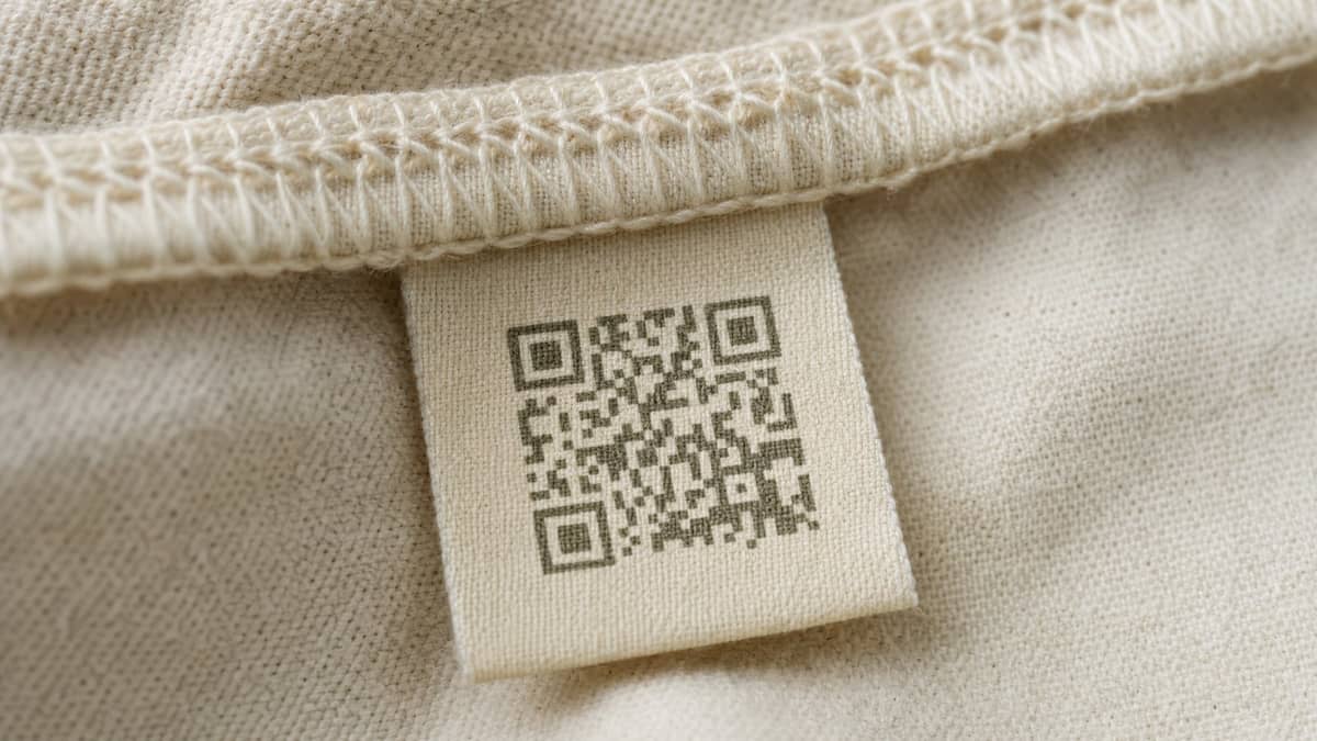 A woven care label carrying a QR code, stitched into the neck seam of a cream organic cotton t-shirt.