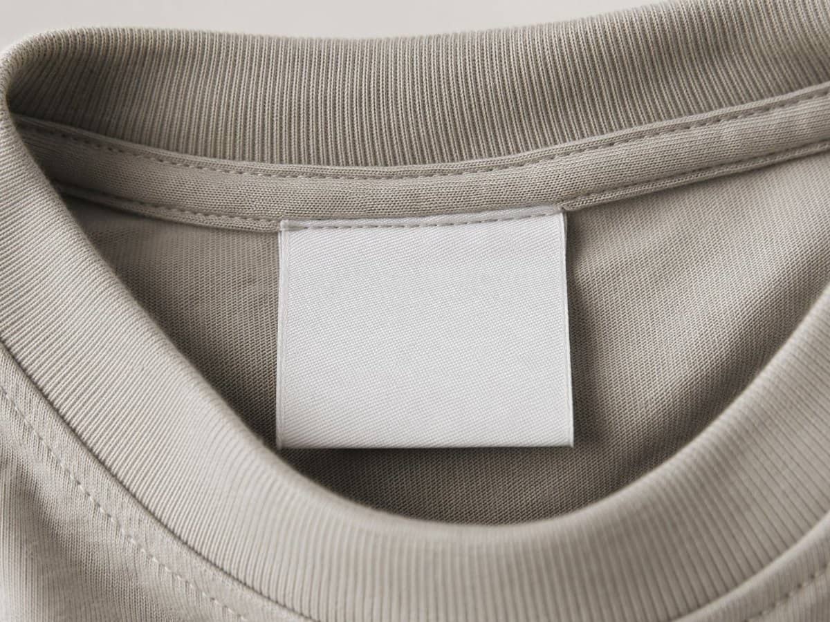 A close-up of a blank white woven neck label sewn into a folded T-shirt collar.