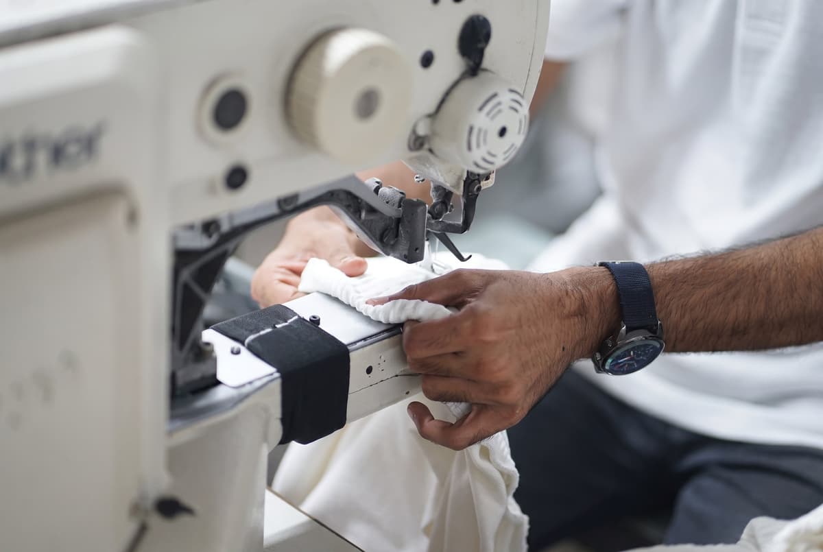 Hands guiding white fabric through a Brother industrial sewing machine at Collective Studio.