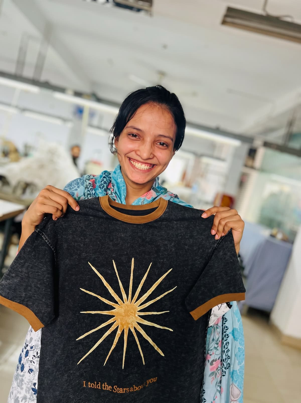 A Collective Studio team member smiling and holding up a finished T-shirt with a gold sunburst print.