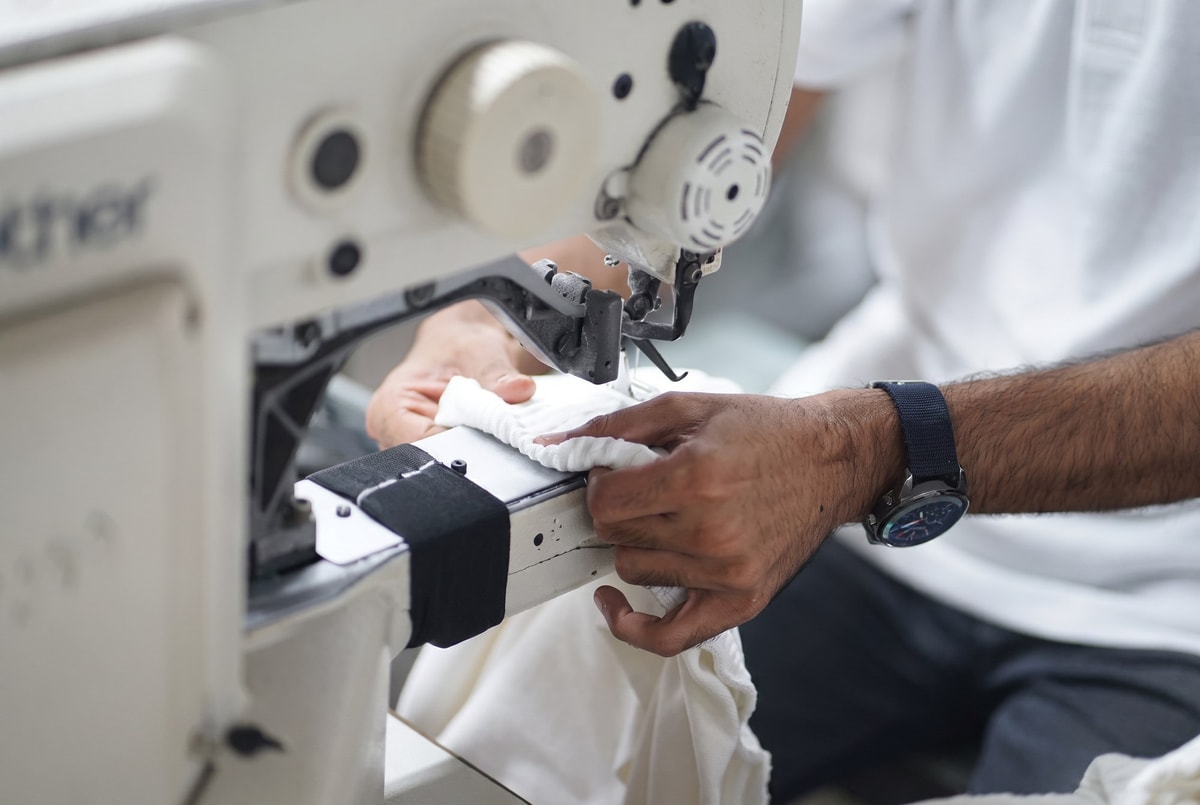 Hands guiding white fabric through an industrial sewing machine.