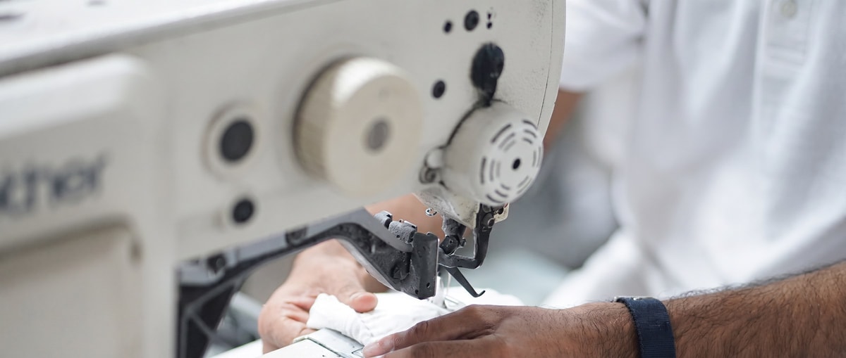 A man works carefully at an industrial cutting machine, fluorescent lights above.