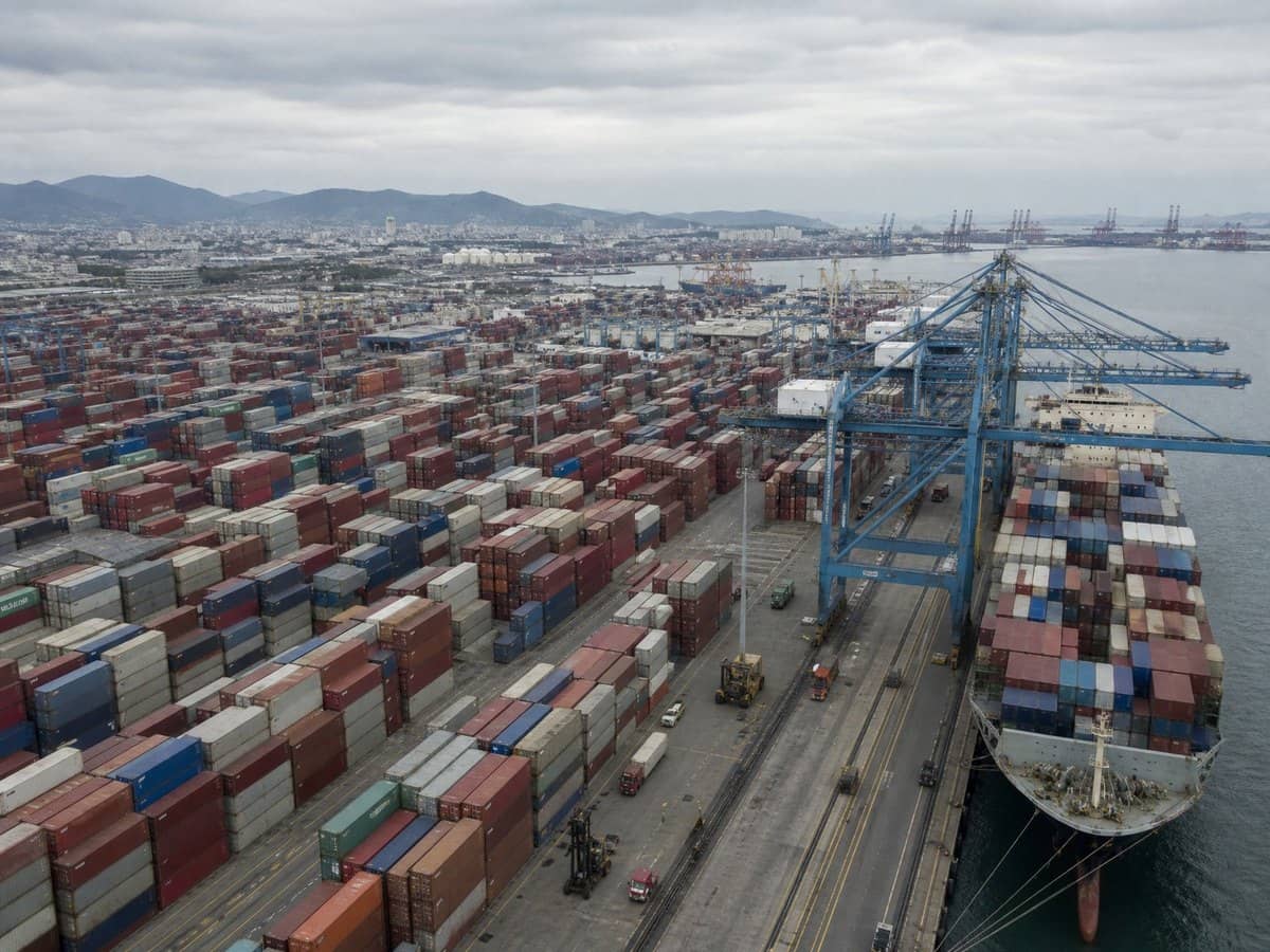 An aerial view of a busy shipping port with stacked cargo containers and a cargo ship.