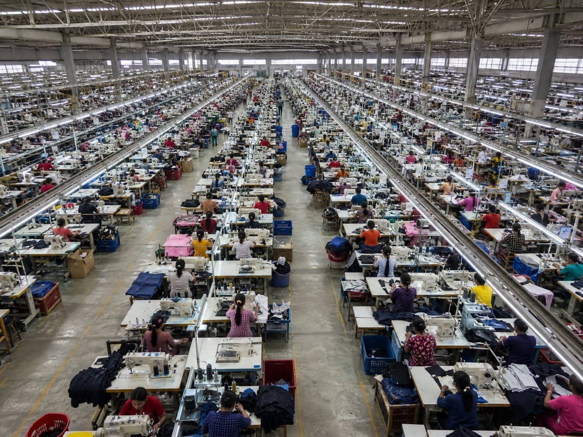 An elevated wide view of a large garment factory floor with dozens of rows of sewing stations.