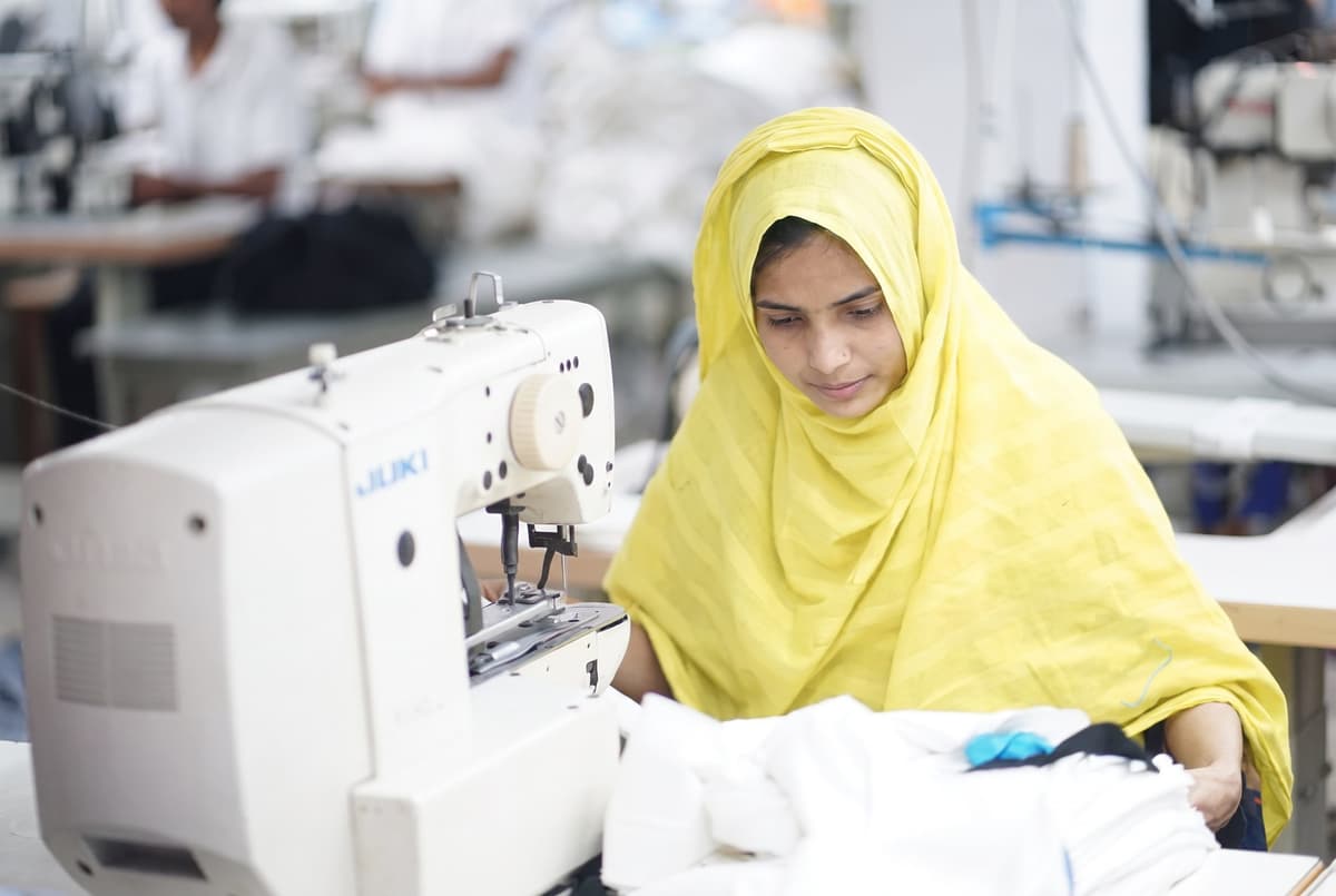 Rashida, a woman in a yellow hijab, focused at a Juki sewing machine at Collective Studio.