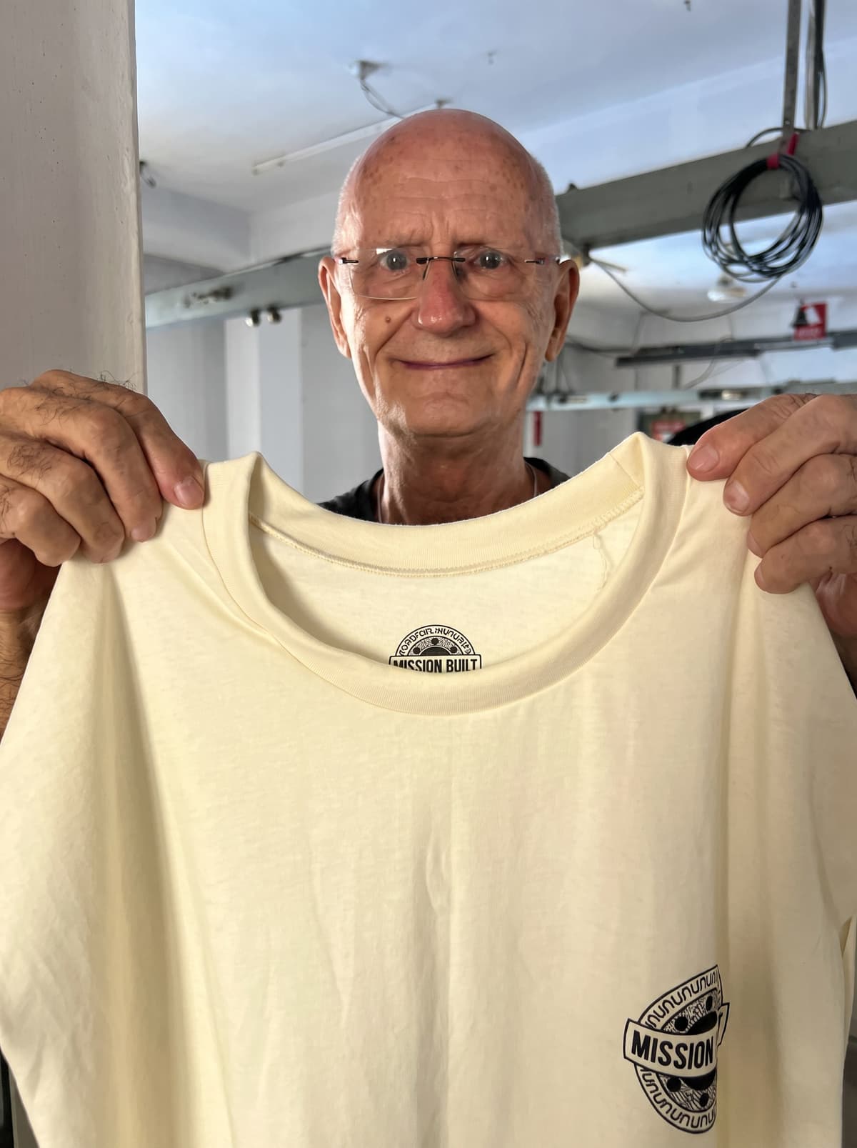 Walter, QC head at Collective Studio, holding up a finished cream T-shirt for inspection.