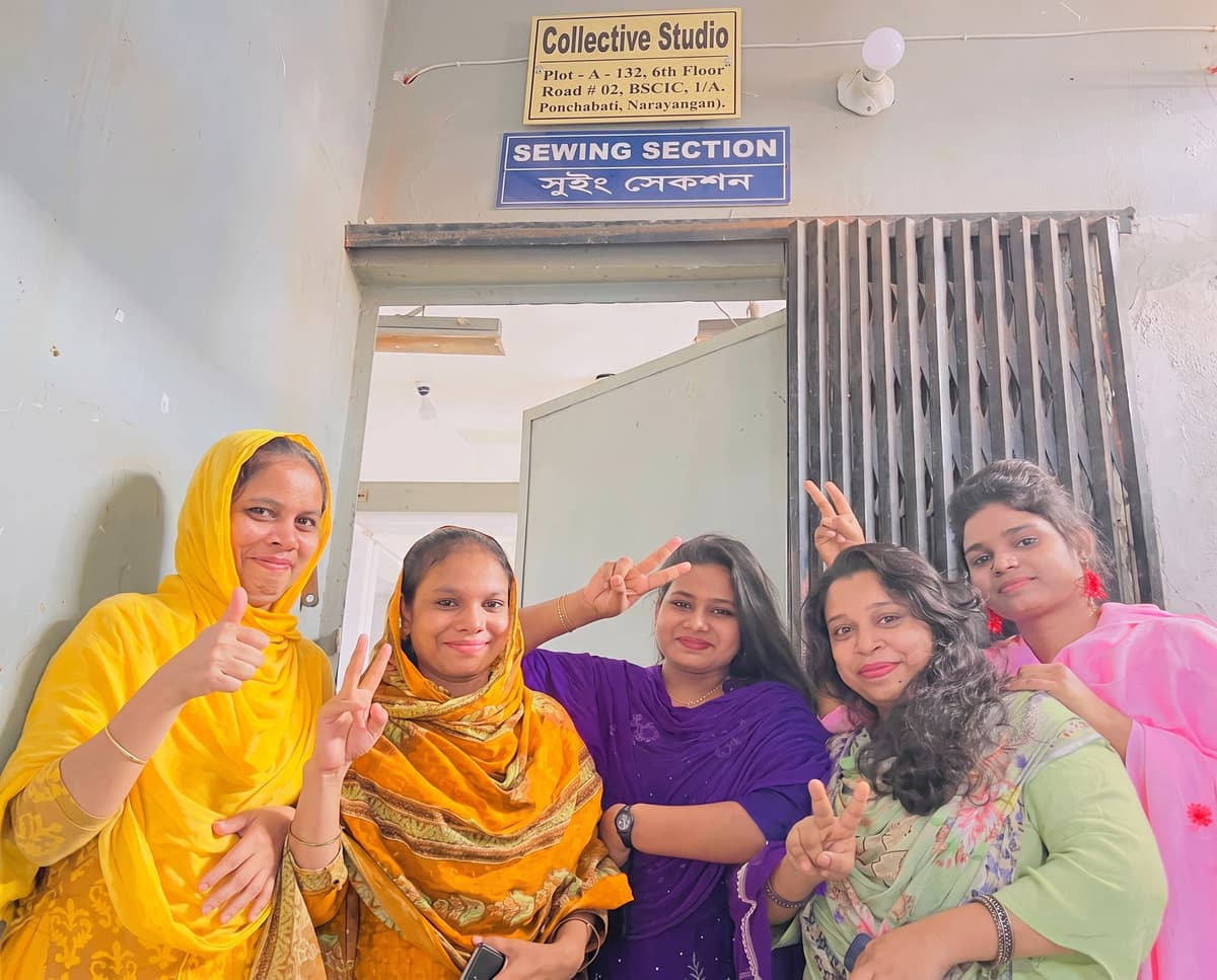 Five women team members pose joyfully under the Collective Studio Sewing Section sign.